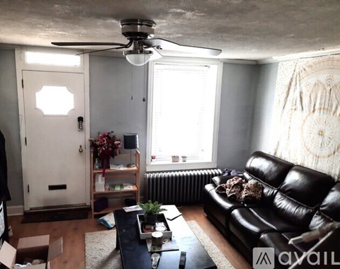 A living room with a black leather couch and a ceiling fan.