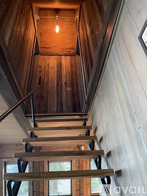 A wooden staircase with a metal railing leads up to a light bulb hanging from the ceiling.
