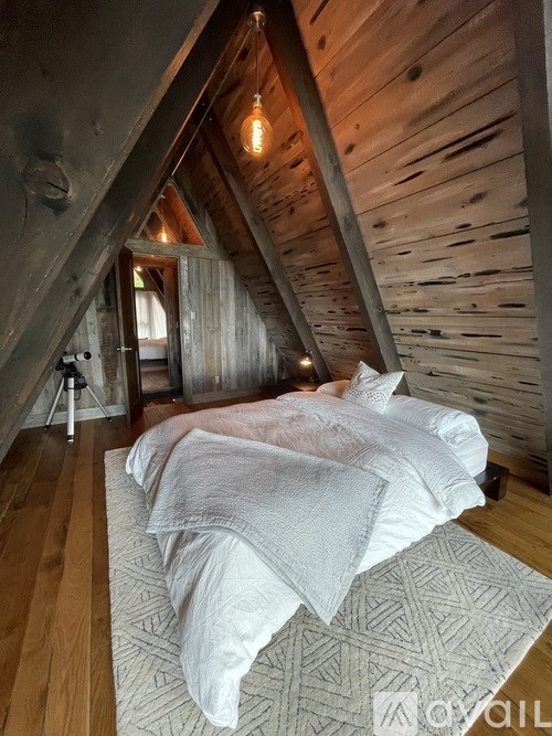 A bed with white bedding is in a room with wooden walls and a wooden floor.