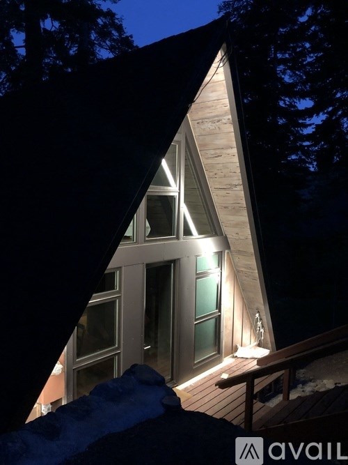 A house with a triangular roof and a deck is lit up at night.