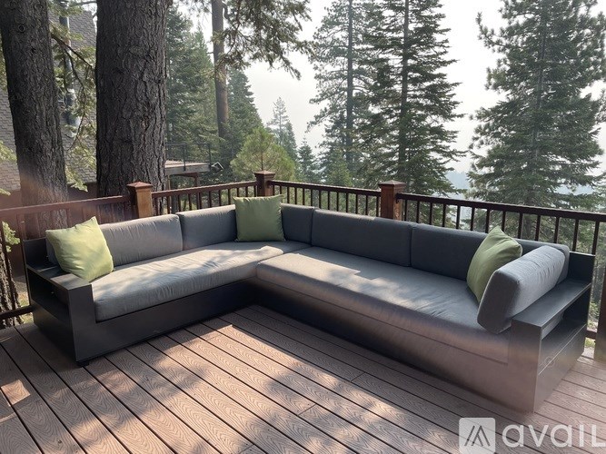 A grey couch with green pillows is on a wooden deck.