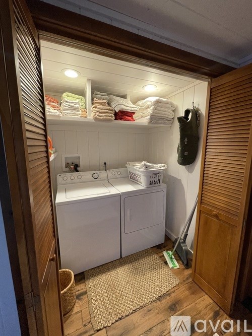 A small laundry room with a washer and dryer, a broom, and towels.