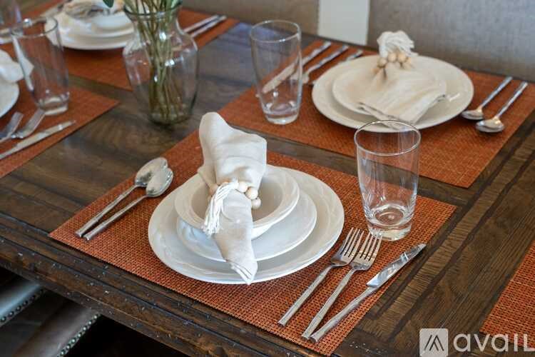 A table set with white plates, silverware, and glasses on a wooden table.
