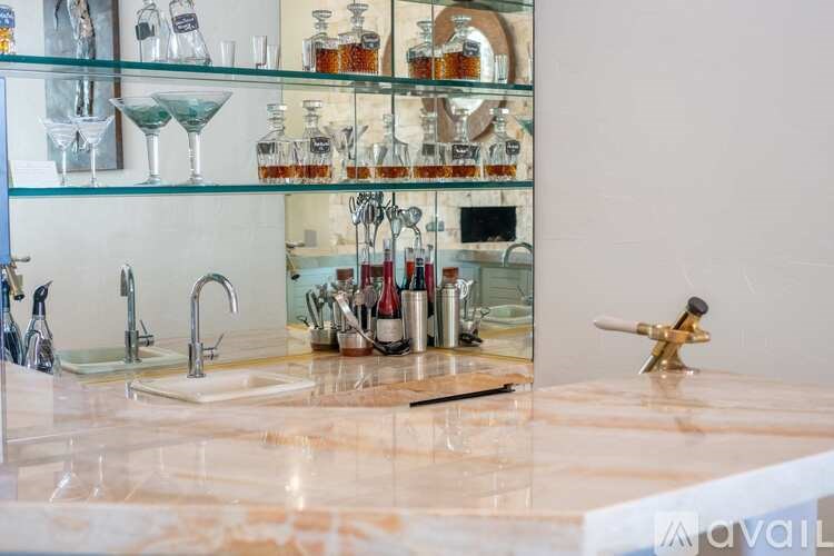 A kitchen counter with a sink and a shelf with glasses and bottles.