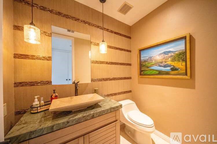 A bathroom with a toilet, sink, and a painting of a landscape.