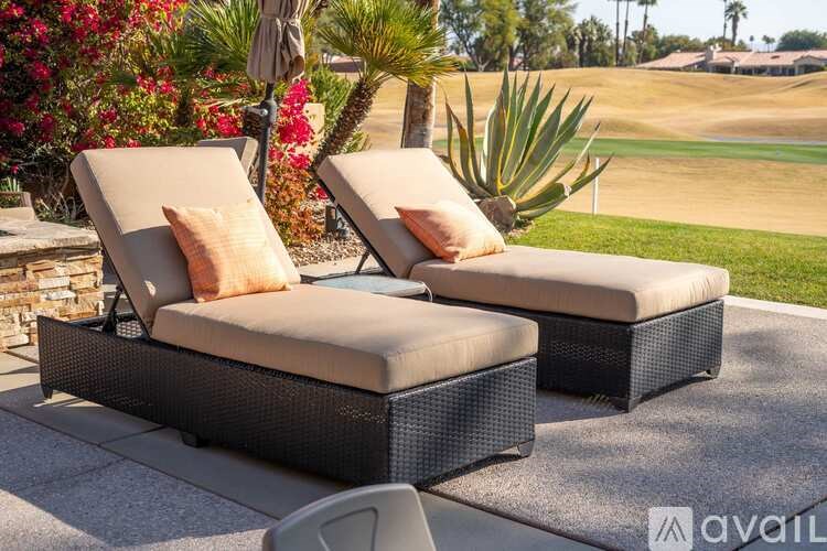 Two wicker lounge chairs with cushions are placed on a patio.