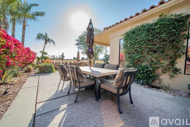 A patio with a table and chairs surrounded by greenery and a statue.