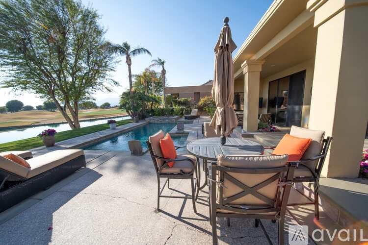 A patio with a table, chairs, and an umbrella overlooking a pool.