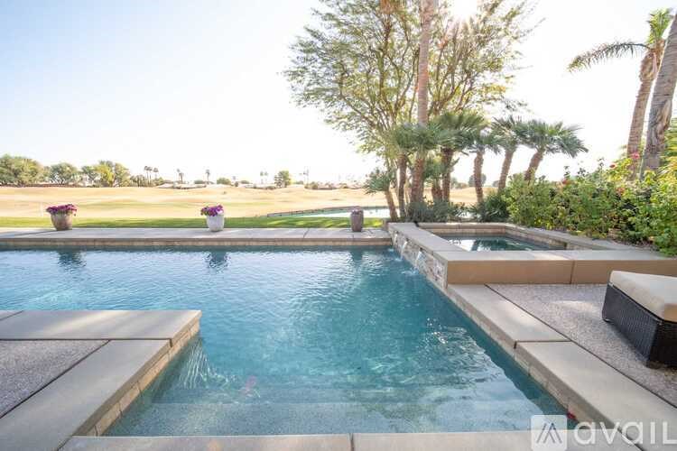A person is swimming in a pool surrounded by a stone ledge and a concrete patio.