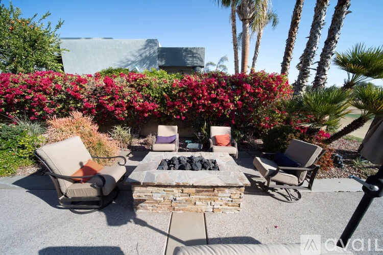 A patio with a fire pit surrounded by chairs and a wall of flowers.