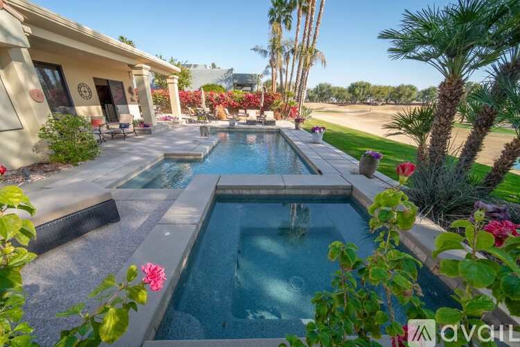 A pool surrounded by plants and a house in the background.