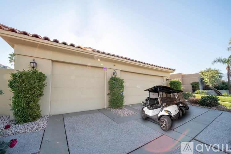 A white golf cart is parked in front of a tan garage.