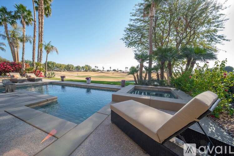 A pool with a sun lounger and palm trees in the background.