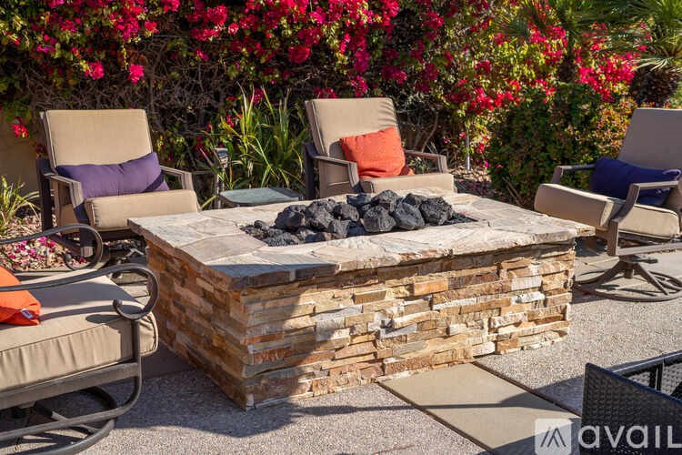 A patio with a fire pit surrounded by chairs and plants.