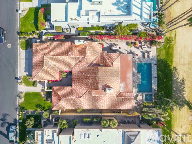A house with a red tiled roof is surrounded by other houses and greenery.