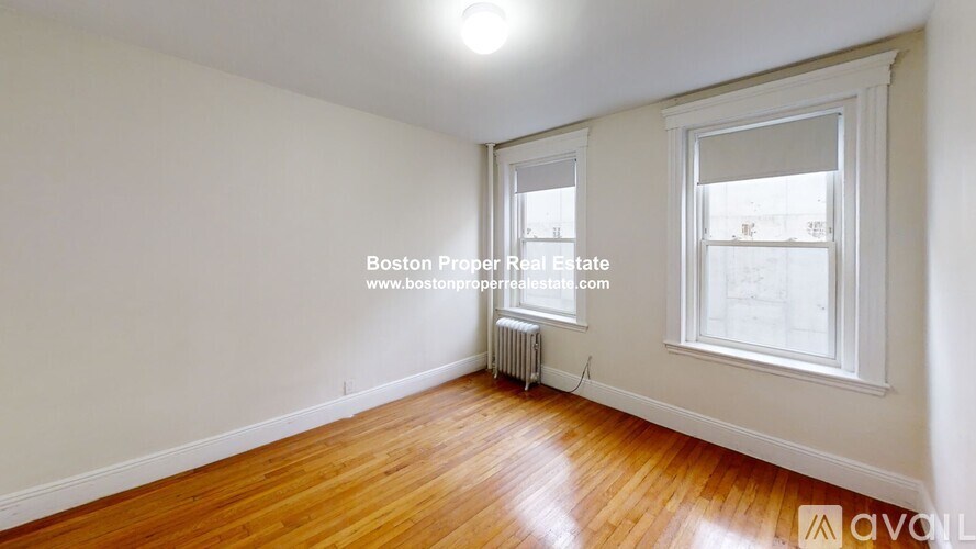 A room with wooden floors and white walls, with a window and a radiator.
