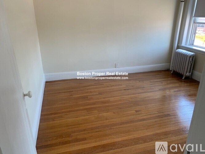 A room with wooden flooring and a window with a radiator.
