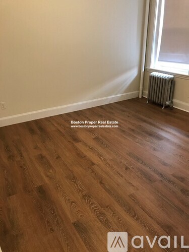 A room with wooden flooring and a window with a radiator to the side.