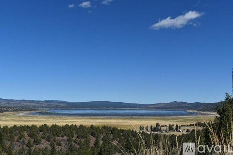 A vast landscape with a lake, sandy beach, and mountains in the distance under a clear blue sky.
