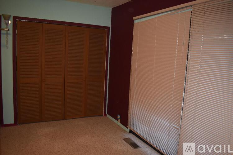 A room with brown wooden closet doors and white blinds on the window.