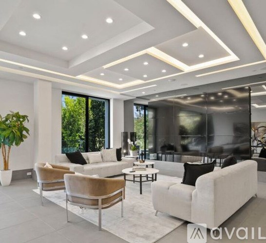 A modern living room with a large white sofa, a glass coffee table, and a large window with a view of trees.