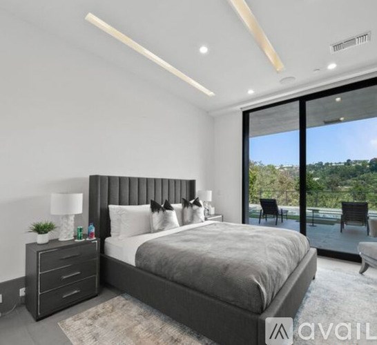 A bedroom with a large bed, a nightstand with a lamp, and a view of the outdoors through a sliding glass door.