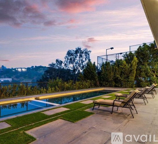 A pool with lounge chairs and a view of the city at dusk.
