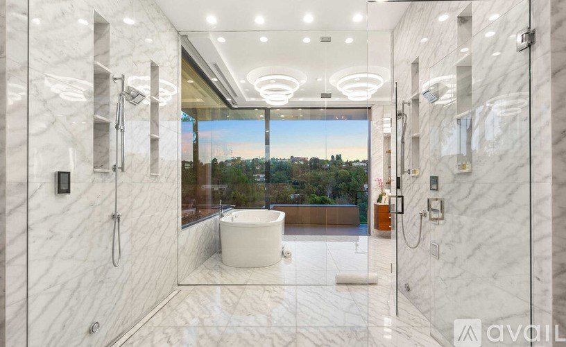 A bathroom with marble walls and floor, a large mirror, and a view of the city through a window.