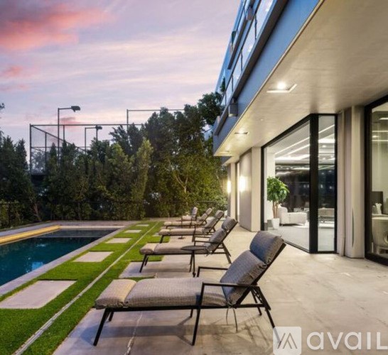 A row of lounge chairs are set up on a patio next to a pool.