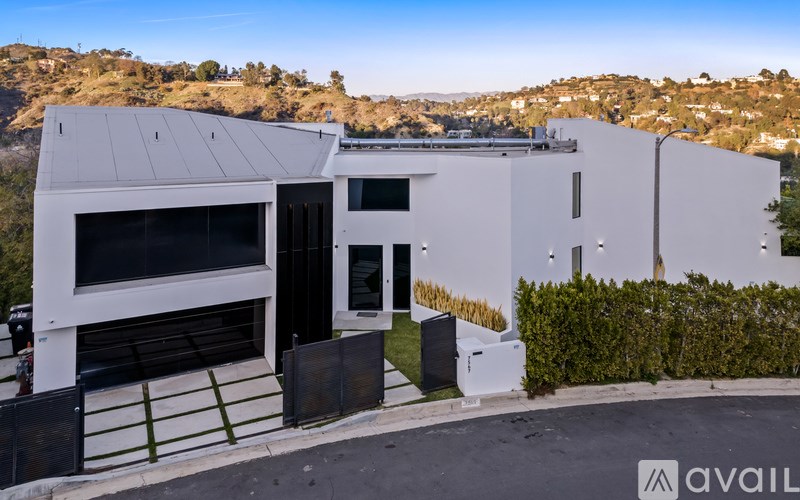 A modern white house with a black gate and a hedge in front.