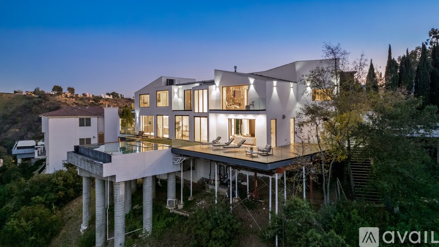 A modern house with a large deck and pillars is available for purchase.