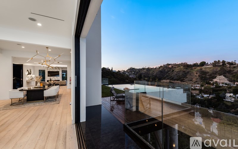 A modern house interior with a glass balcony overlooking a hilly landscape.