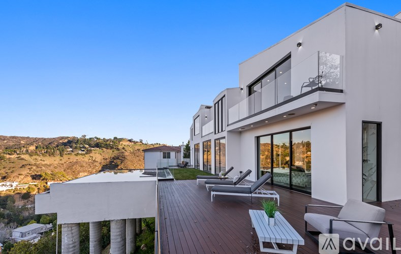 A modern house with a balcony and lounge chairs on the deck.