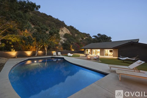 A swimming pool in a backyard with a house and trees in the background.
