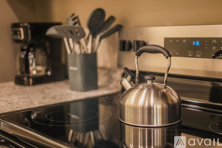 A silver kettle on a stove with a set of utensils in a holder to the left.