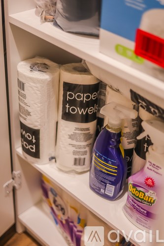 A white shelf with toilet paper, paper towels, and cleaning supplies.