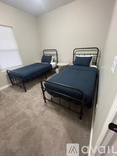 Two beds in a room with carpeted floor and white walls.