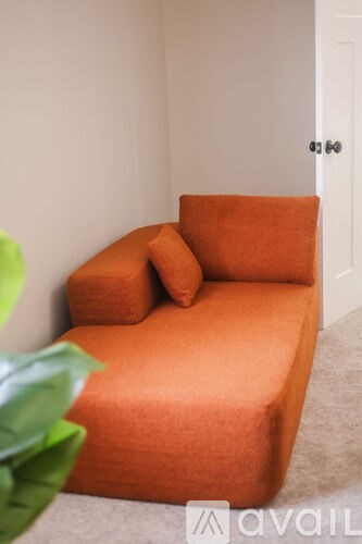 A small orange sofa with a pillow on it.