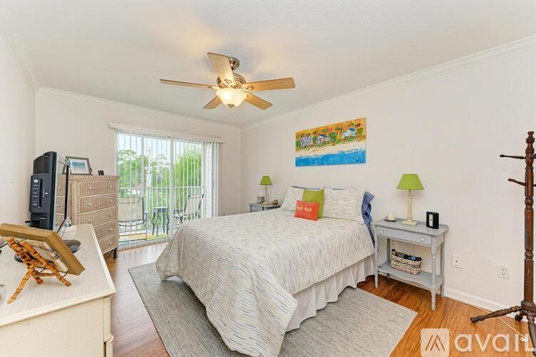 A bedroom with a bed, a ceiling fan, and a painting on the wall.