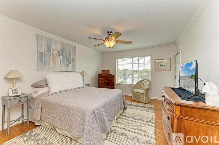 A bedroom with a bed, a chair, a ceiling fan, and a television.