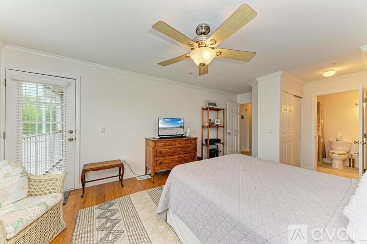 A bedroom with a bed, a chair, a television, and a ceiling fan.