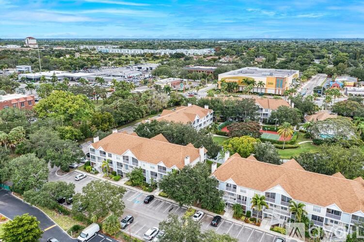 A large white building with a brown roof is surrounded by trees and has a parking lot in front.