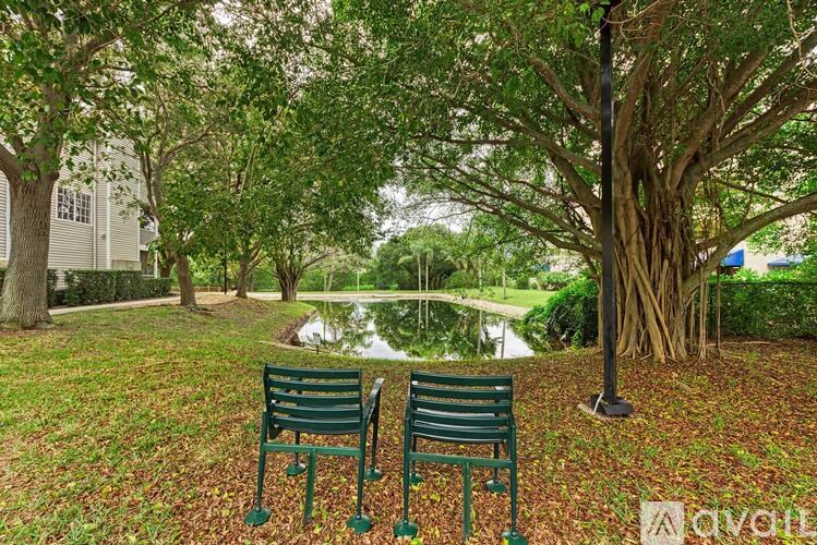 Two green benches are placed on a grassy area with trees and a pond in the background.
