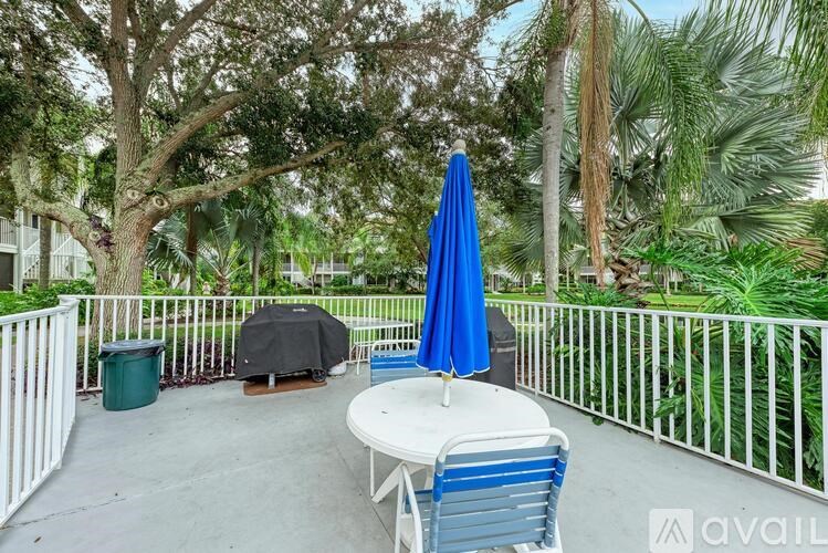 A patio with a white table and blue chairs is surrounded by a white fence and has a blue umbrella.