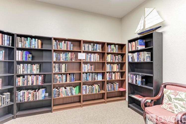 A room with a bookshelf filled with books and a chair with a cushion.