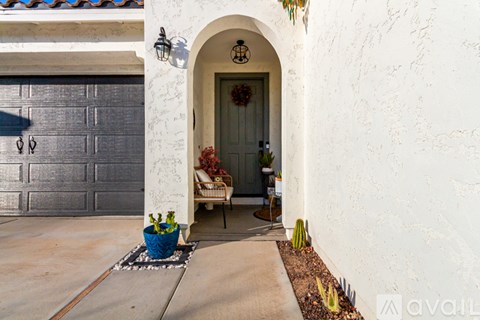 A white house with a grey garage door and a blue planter on the concrete.