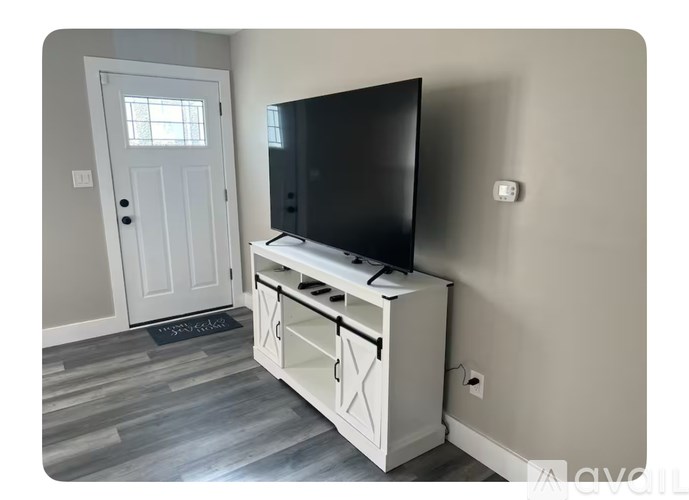 A black television sits on a white cabinet in a room with a grey door.