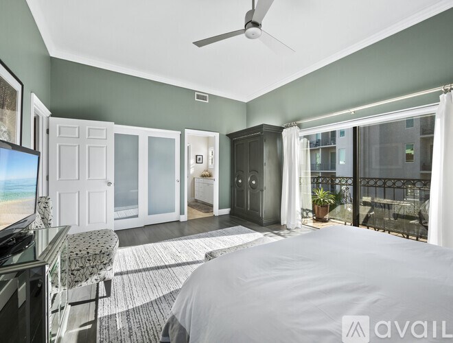 A bedroom with a bed, a chair, a ceiling fan, and a balcony with a view of the city.