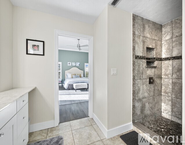 A bathroom with a walk-in shower and a bedroom visible through the glass door.