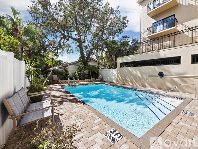 A small pool surrounded by a brick patio and a white fence.